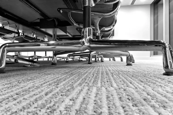 Low view of commercial carpet beneath a row of chrome office chairs